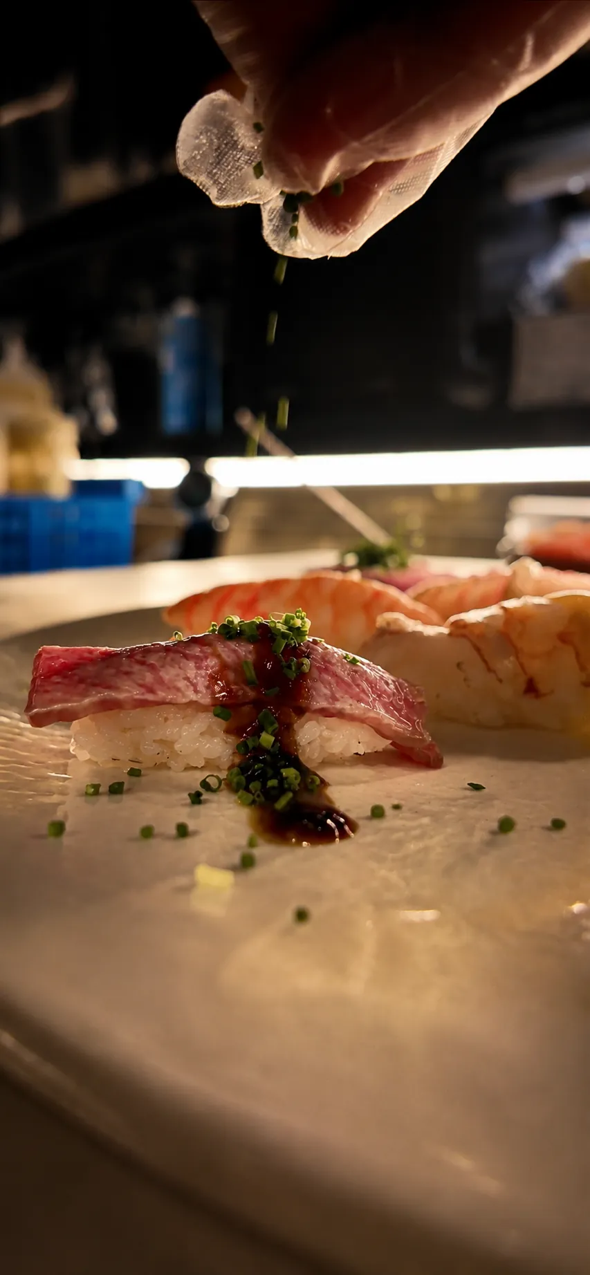 La mano dello chef lascia cadere erba cipollina sul nigiri